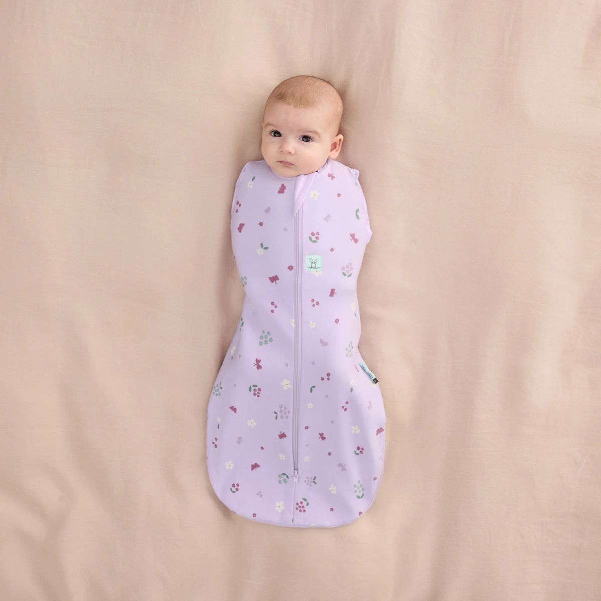 Baby wrapped in a purple sleeping bag with floral pattern on a beige background